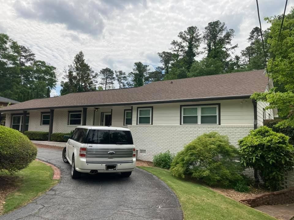 A white SUV parked in the driveway of a single-story, white-sided house with a brown roof.