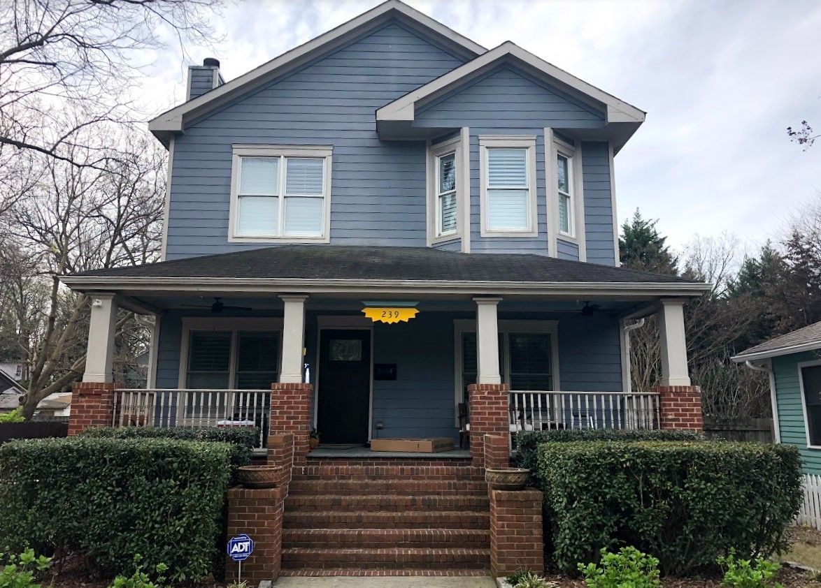 Blue two-story house with porch, brick steps, and green bushes.