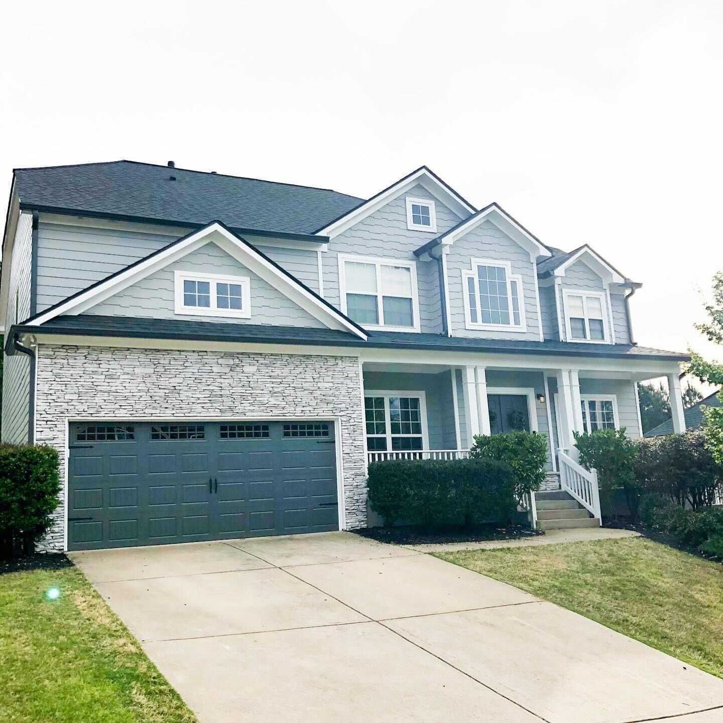 Two-story gray house with a gray garage door and a stone facade next to it. Green lawn and driveway in front.
