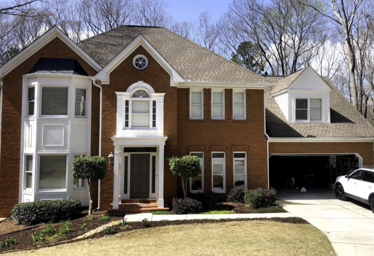Two-story brick house with white trim, a brown roof, and a driveway with a car.