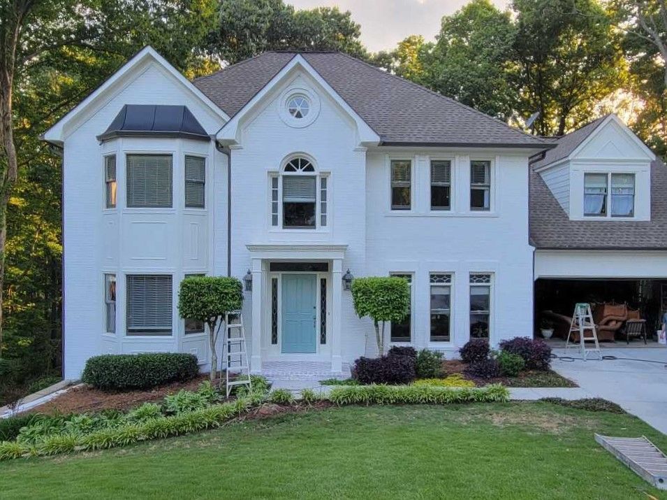 White two-story house with teal front door, brown roof, and well-manicured landscaping.