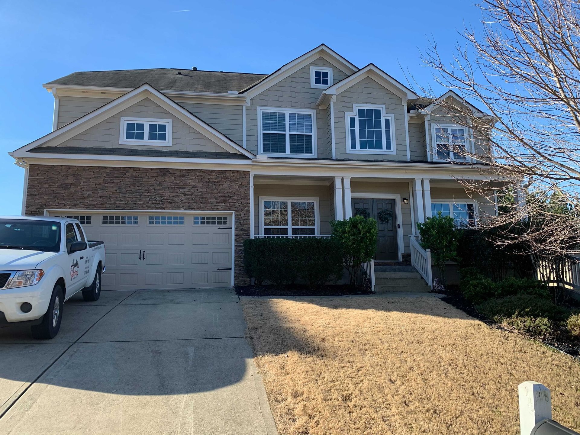 Two-story beige house with brick accents, front porch, and a white work truck parked in the driveway.