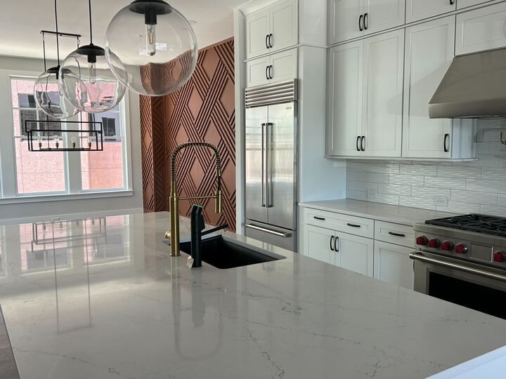 Modern kitchen with white cabinets, large island, stainless steel appliances, and decorative wall.