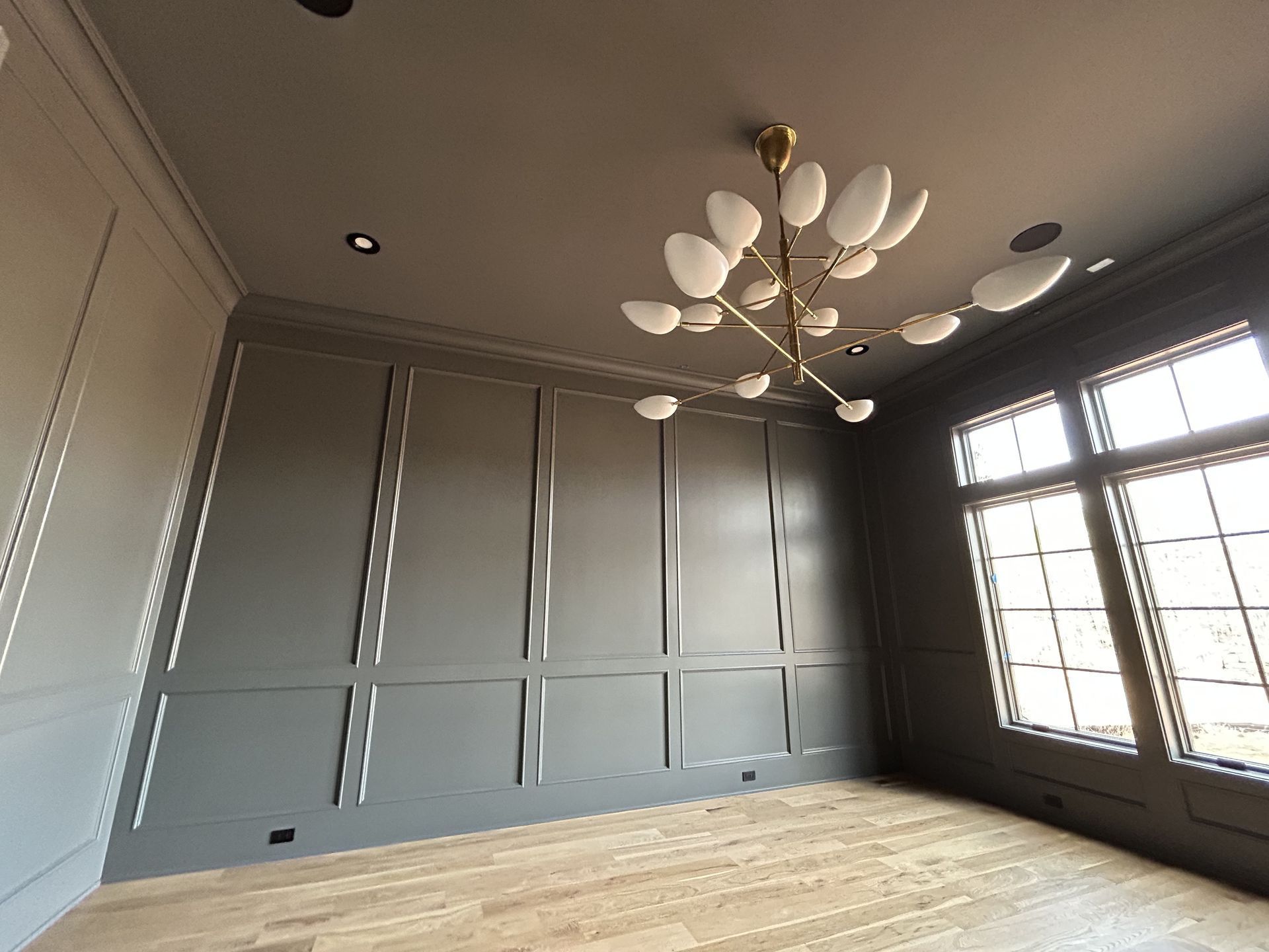 Empty room with gray paneled walls, wood floor, and a modern chandelier.