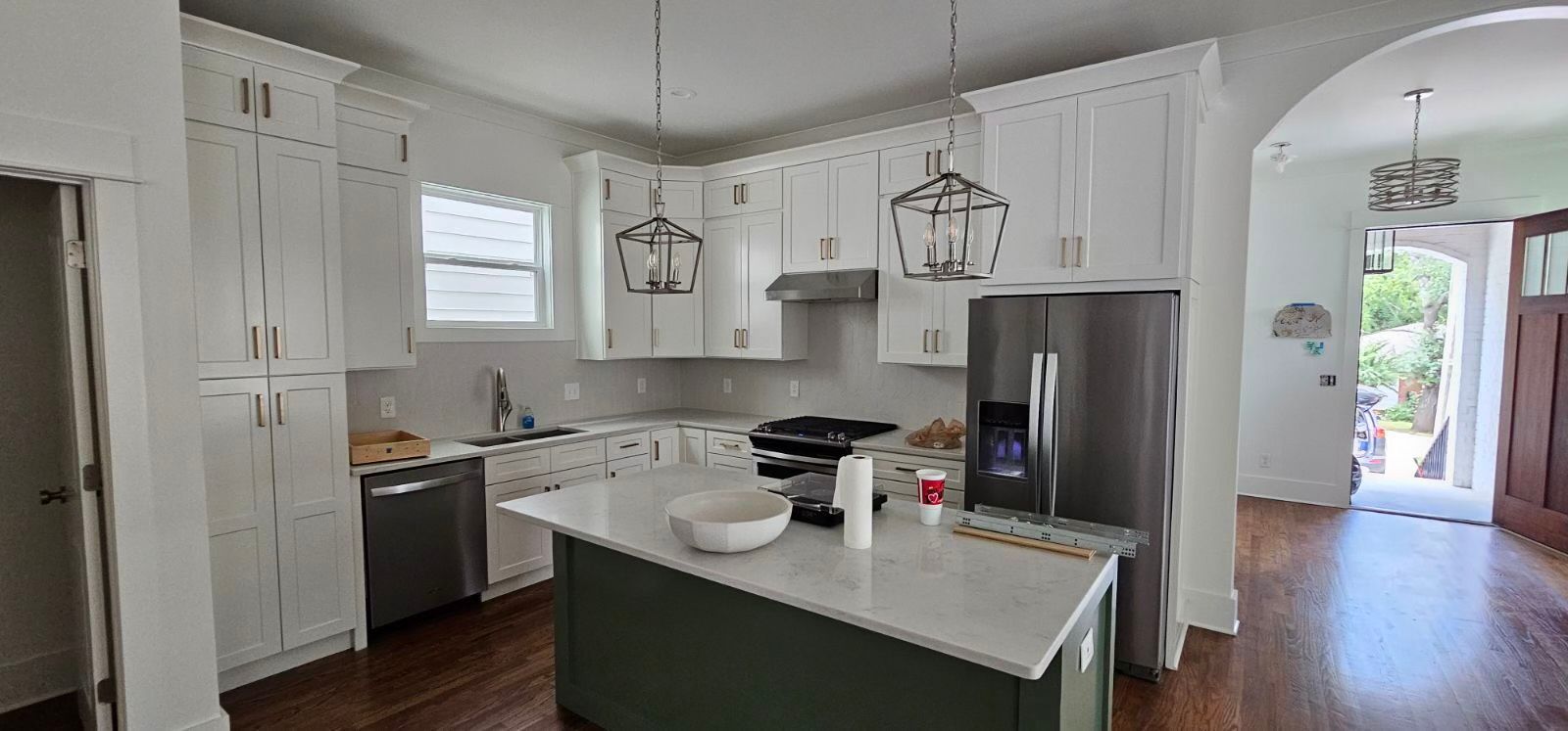 A modern kitchen with white cabinets, stainless steel appliances, and a green island. Wooden floor and an archway.