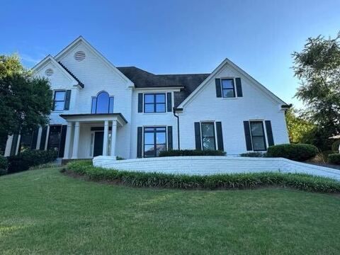 White two-story house with black shutters, blue sky, and green lawn.