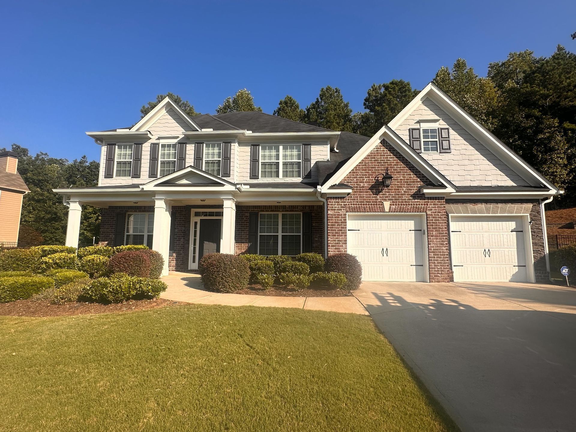 Two-story house with light siding, brick accents, white trim, three-car garage, and a green lawn.