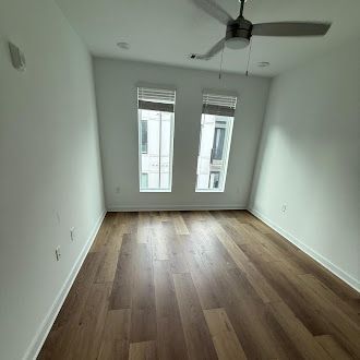 Empty room with hardwood floors, two windows, and a ceiling fan.