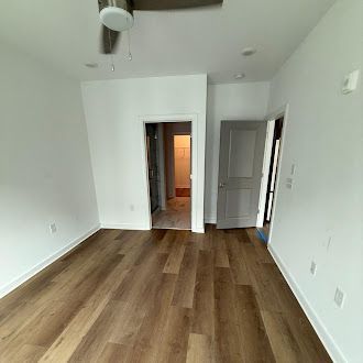 Empty bedroom with wood-look floor, white walls, two doorways, and a ceiling fan.