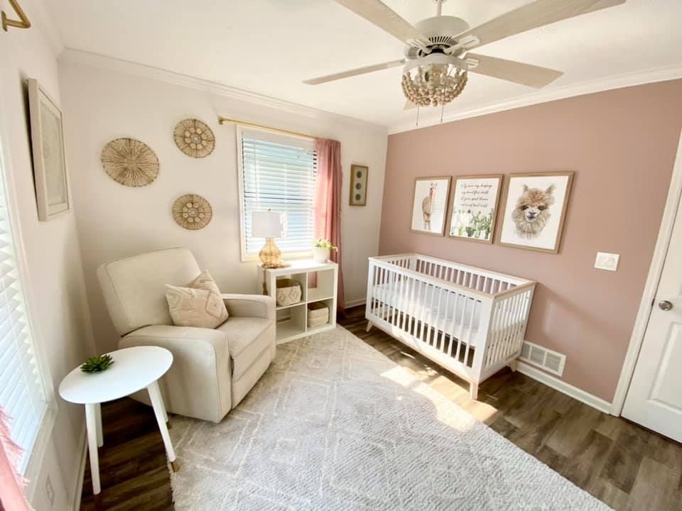 A nursery with a crib , chair , table and ceiling fan.