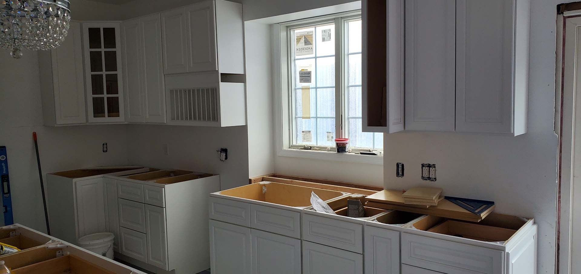 A kitchen under construction with white cabinets and a window.