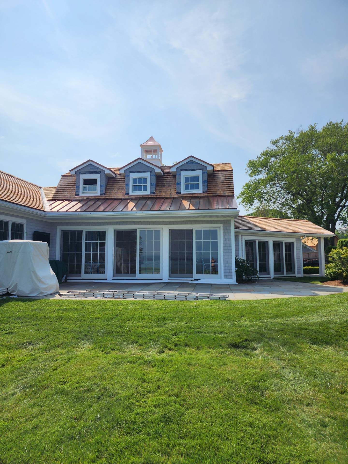 A large white house with a copper roof is sitting on top of a lush green lawn.