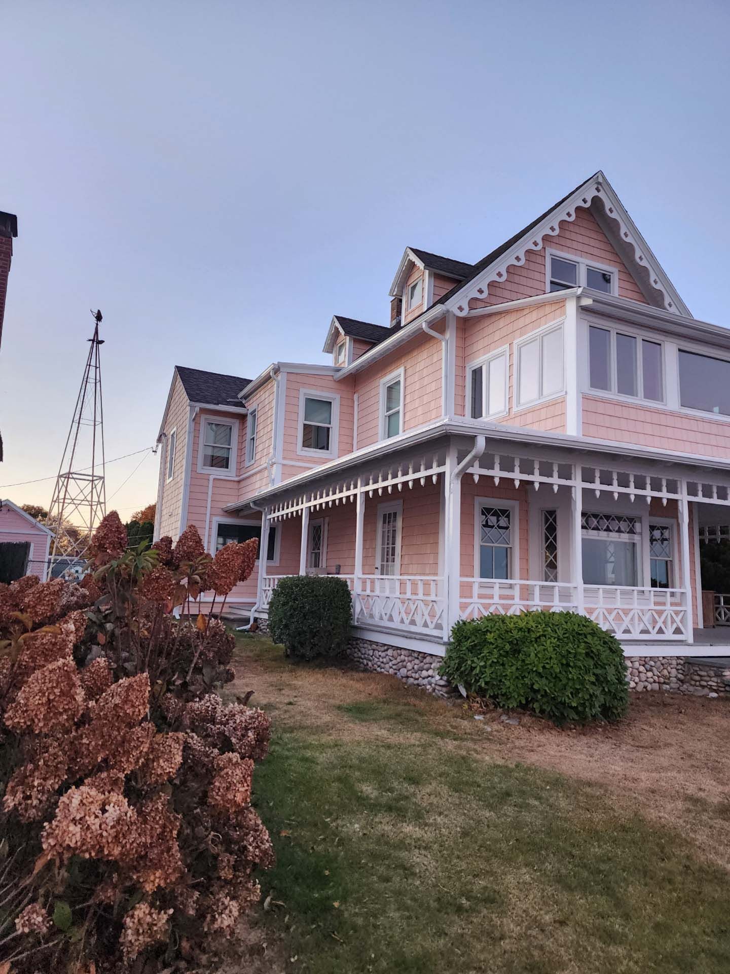 A large pink house with a large porch is sitting on top of a lush green field.
