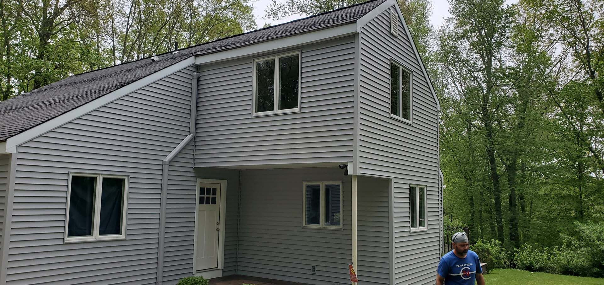 A man in a blue shirt is standing in front of a white house.