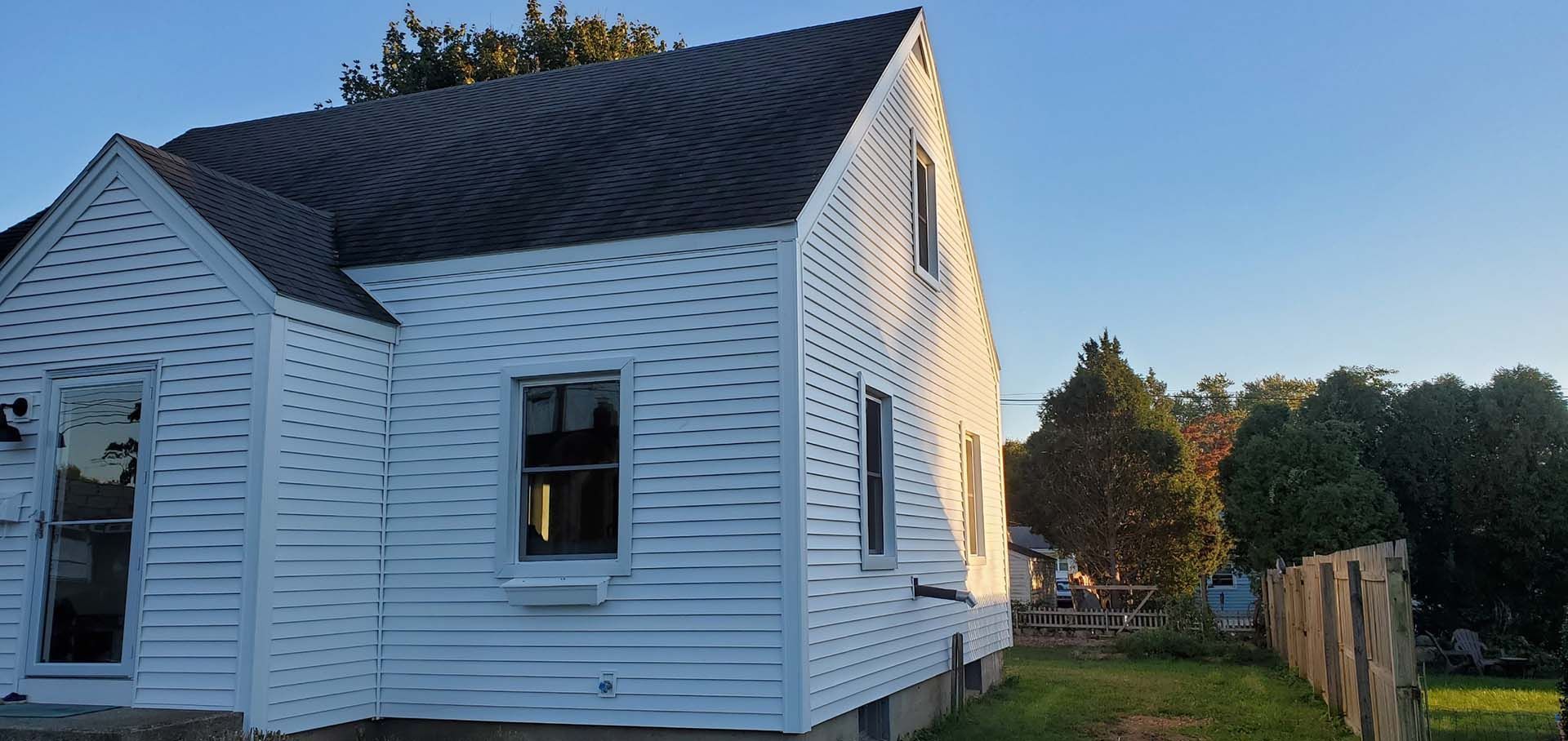A white house with a black roof and a fence in front of it