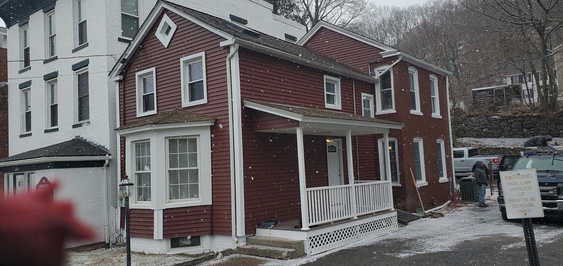 A red and white brick house with a porch in the snow.