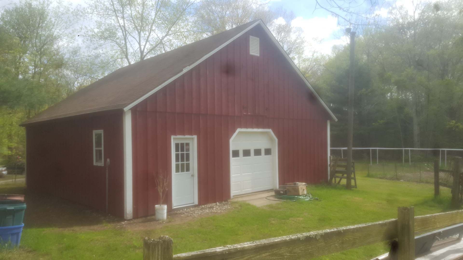 A red barn with a white garage door is sitting in the middle of a grassy field.