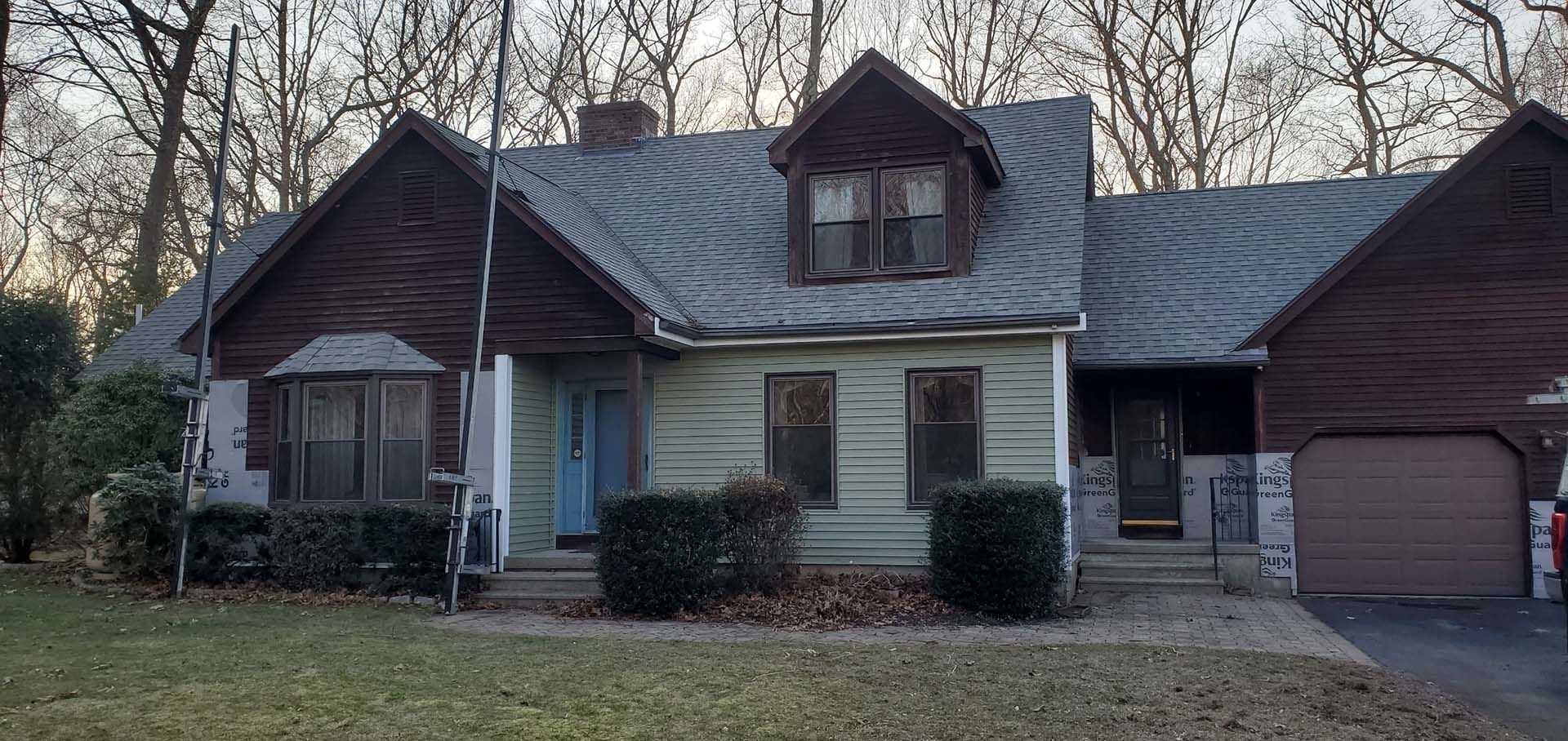 A white house with a brown roof and a garage is surrounded by trees.