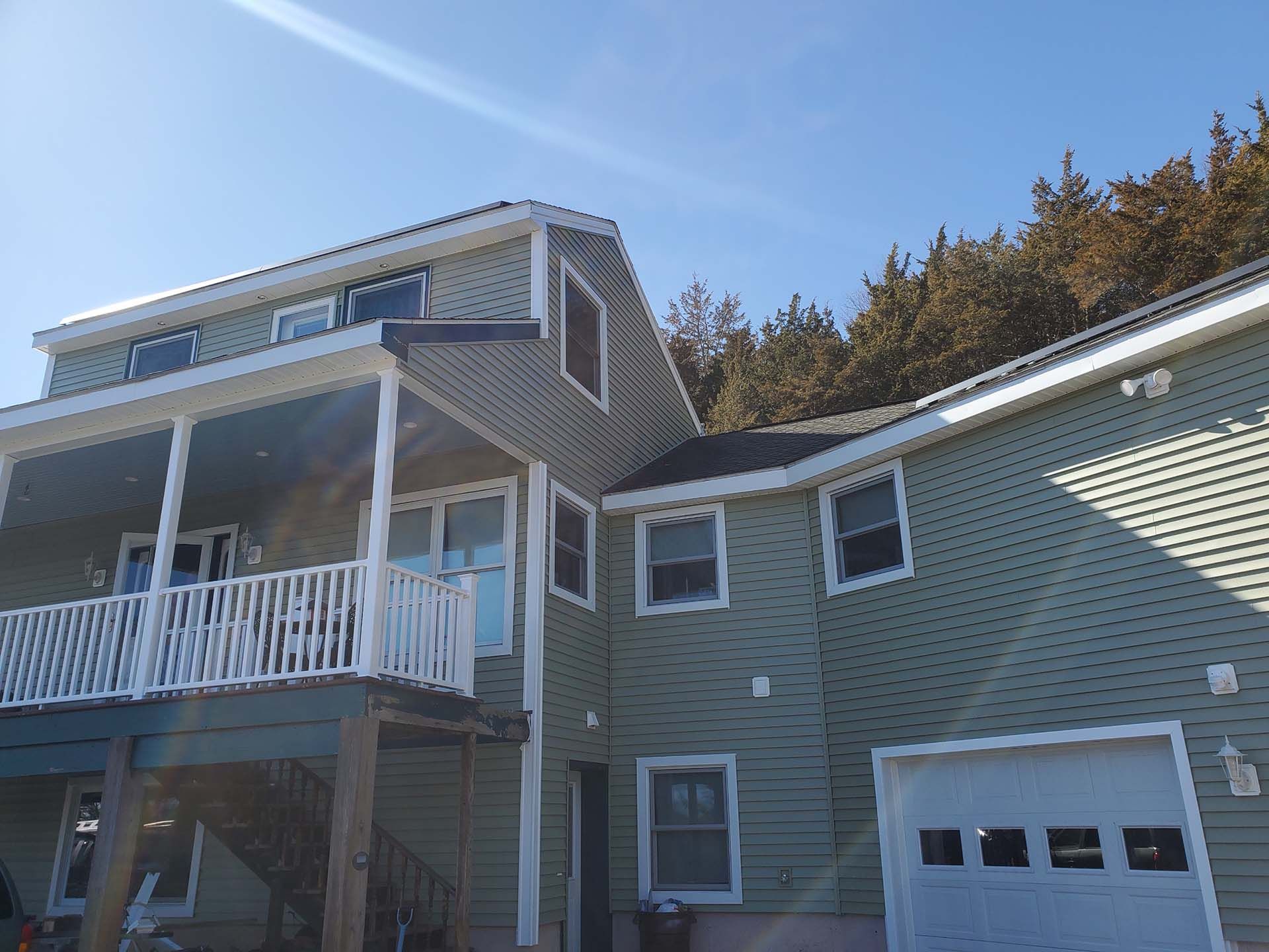 A large green house with a white porch and a garage.