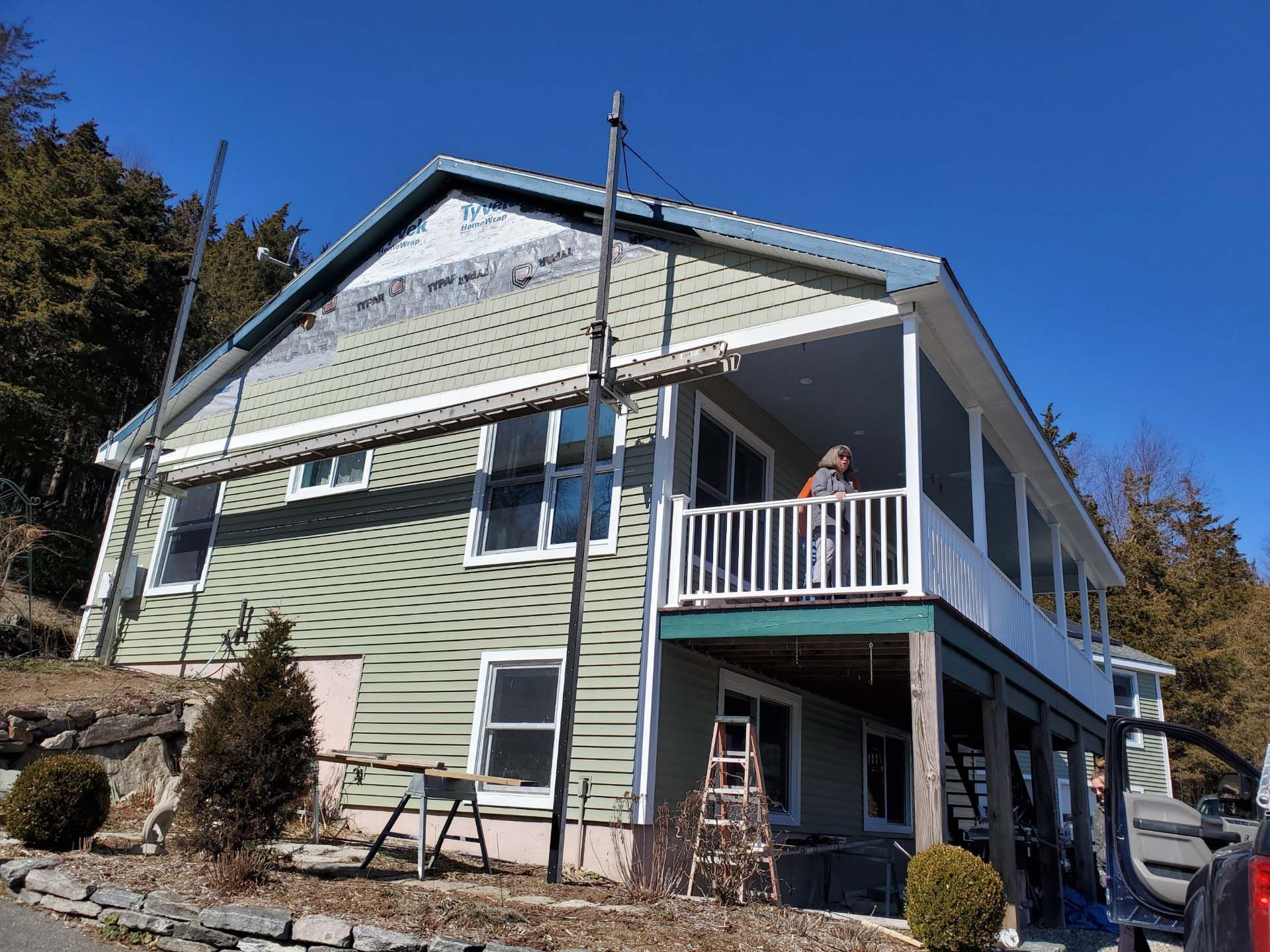 A large green house with a white porch is being remodeled.