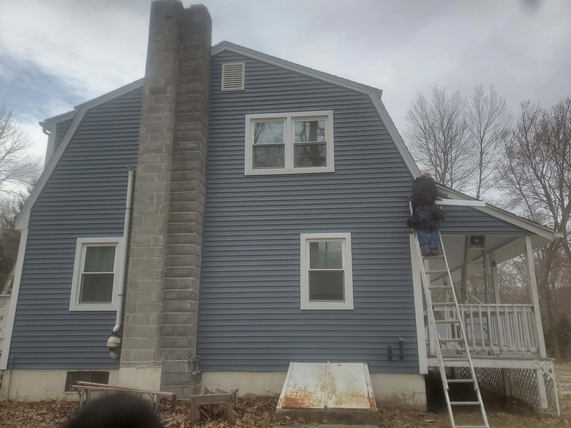 A man is standing on a ladder on the side of a blue house.
