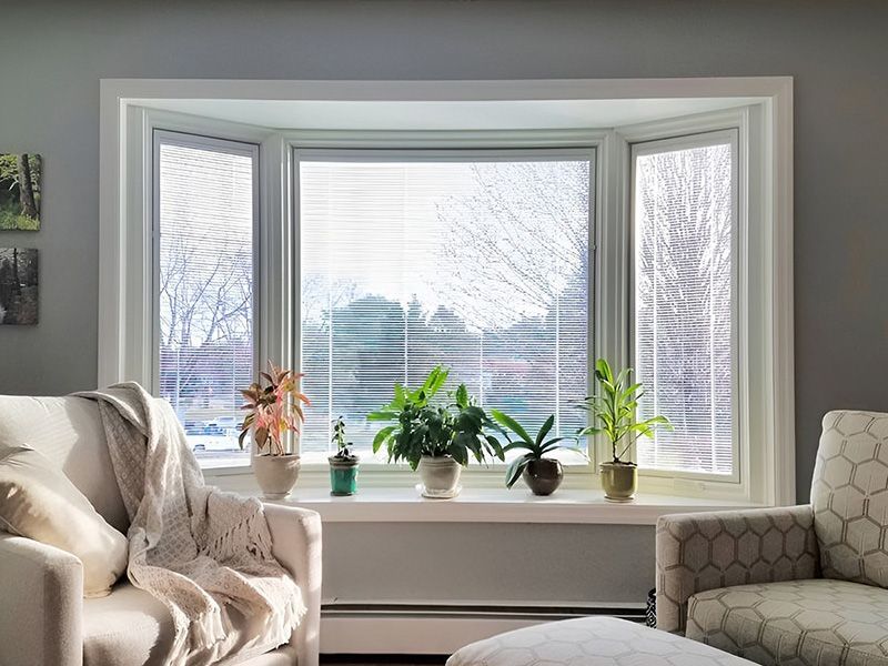 A living room with a large bay window and plants on the window sill.