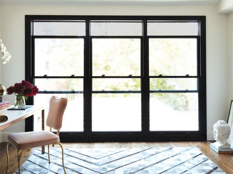 A room with a desk , chair , rug and a large window.