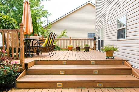 A wooden deck with stairs and a table and chairs in front of a house.