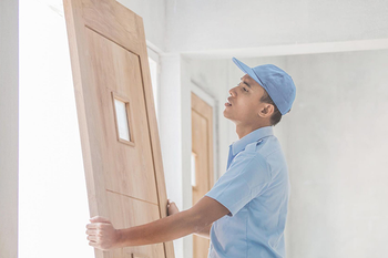 A man in a blue shirt and hat is holding a wooden door.