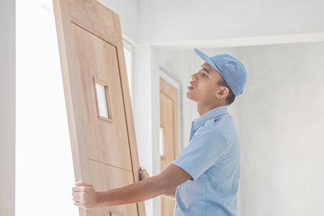 A man in a blue shirt and hat is holding a wooden door.
