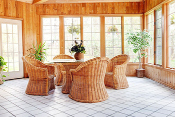 There is a table and chairs in the sunroom with lots of windows.