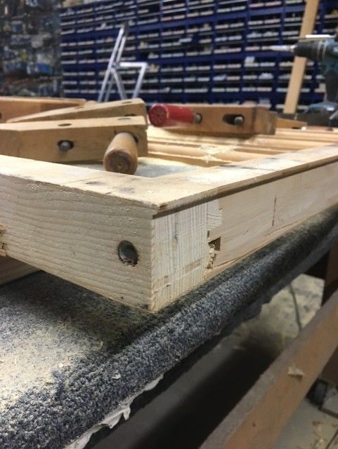 A wood project corner showing a joinery detail with a dowel, clamped on a workbench in a workshop.