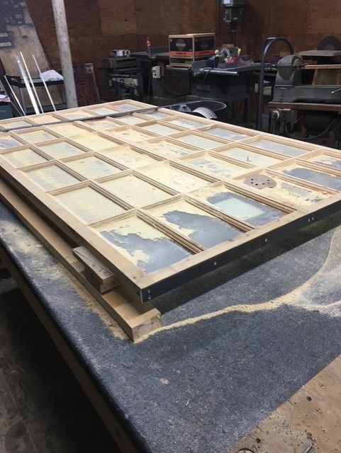 A large rectangular wooden grid frame sits on a workbench in a cluttered workshop.