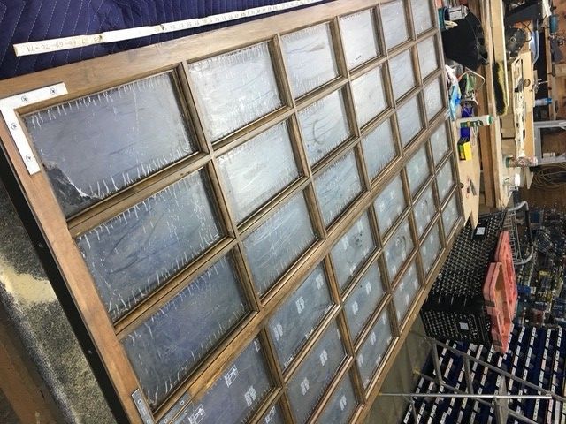 A large, multi-paneled wooden window frame lying on a workbench in a workshop.