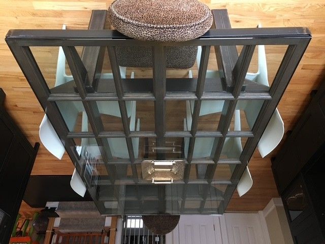 Top-down view of a rectangular dining table with a multi-pane glass top and dark wooden frame, surrounded by white chairs.