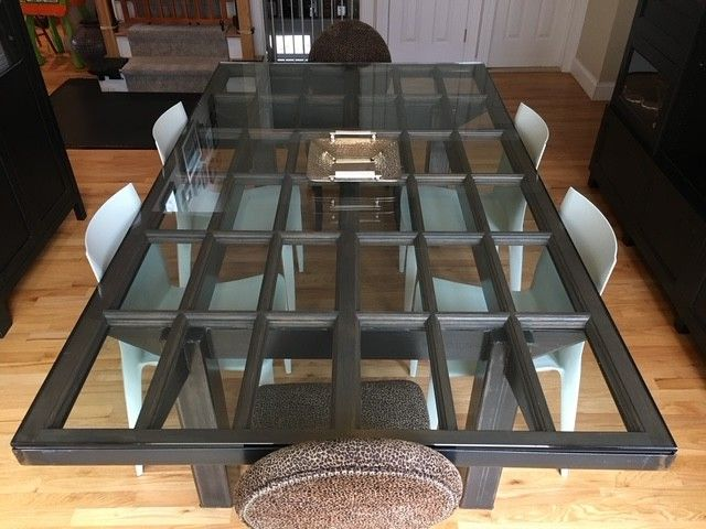 Top-down view of a rectangular dining table with a multi-pane glass top and dark wooden frame, surrounded by white chairs.