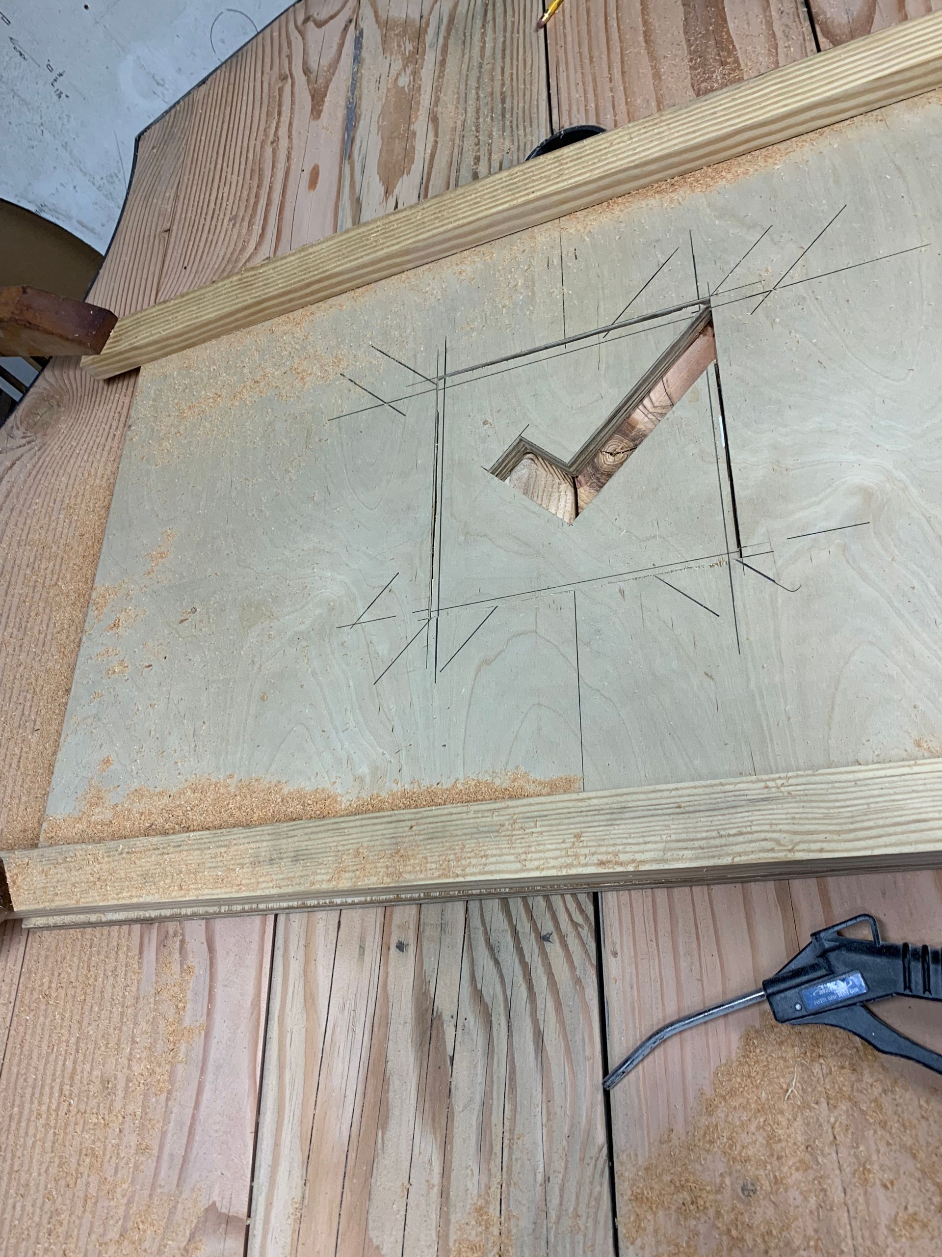 A piece of plywood with a V-shaped cut-out, marked with pencil lines and sawdust on a wooden workbench.