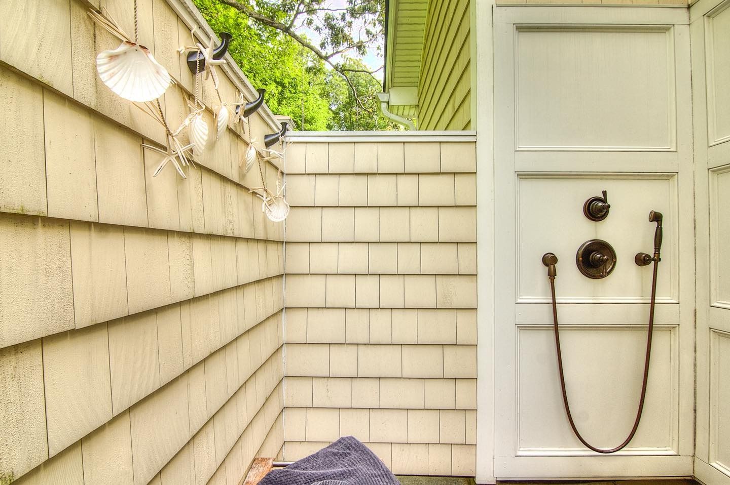 Outdoor shower with white wooden door and light-colored shingles.  Decorative seashell string lights.