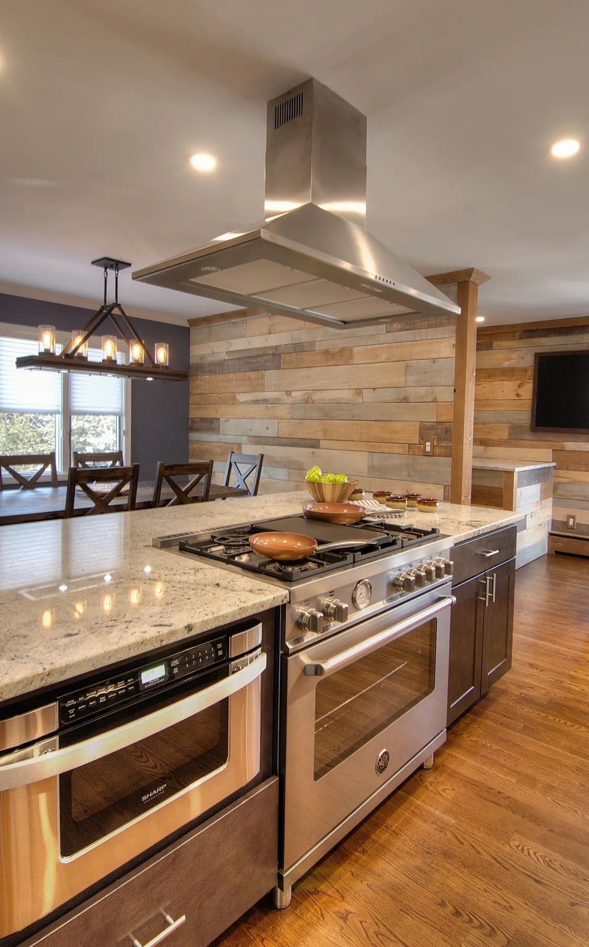 Modern kitchen with island, stainless steel appliances, and wood accent wall.