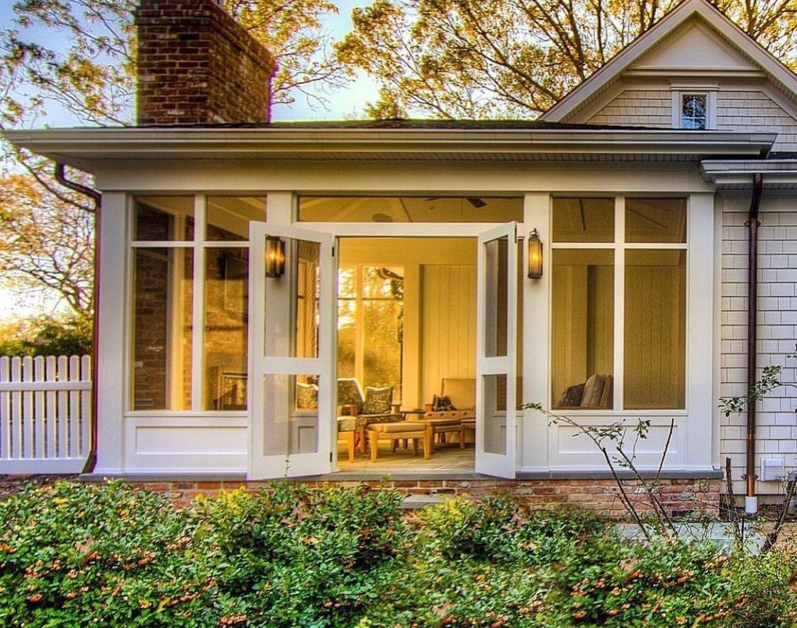 Screened-in porch with white trim and French doors, leading to a warmly lit interior. Brick chimney.
