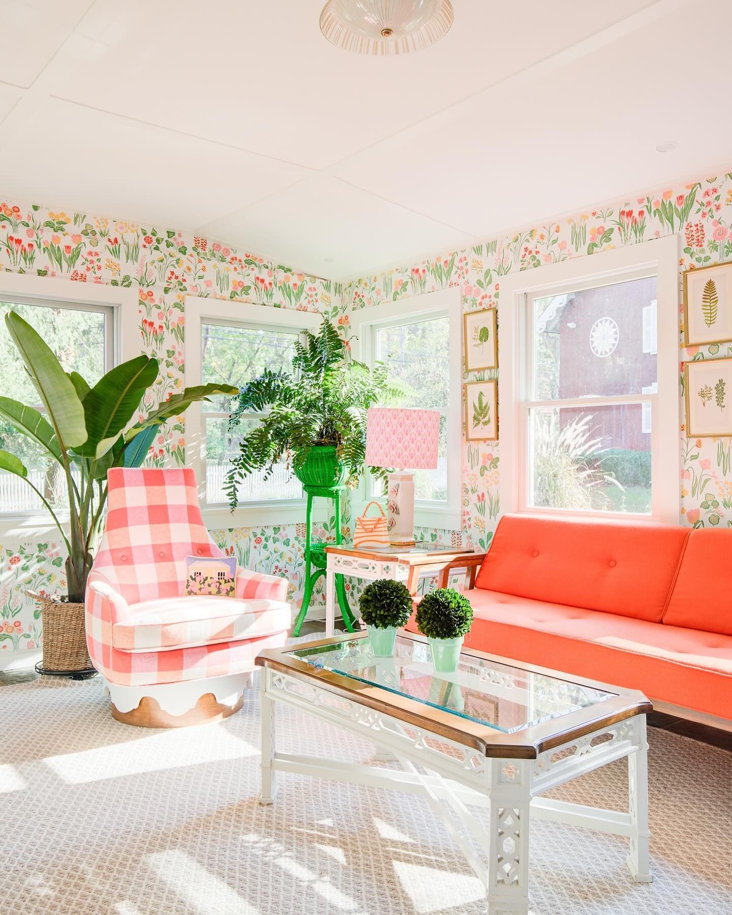 Sunroom with floral wallpaper, gingham armchair, orange sofa, and glass coffee table.