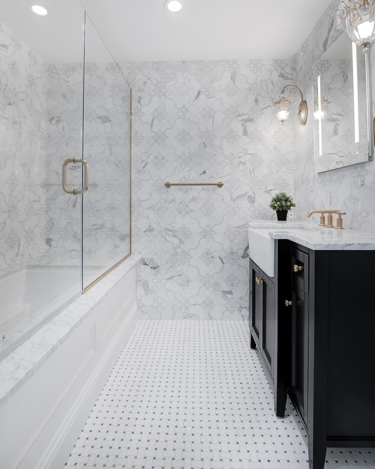 Elegant marble bathroom with black vanity, tub, glass shower door, and white tile floor.