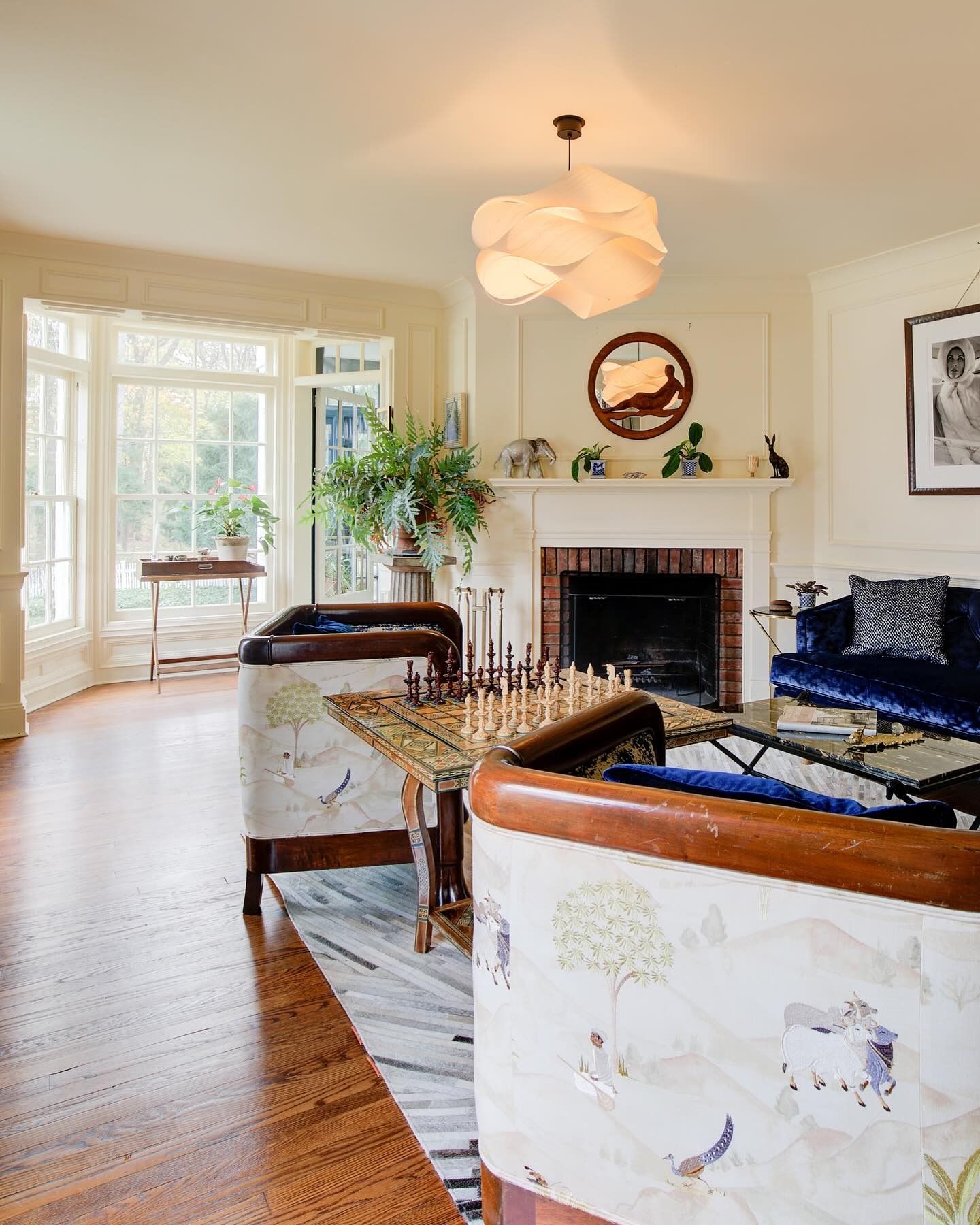 Living room with white walls, bay windows, fireplace, patterned furniture, and a modern light fixture.