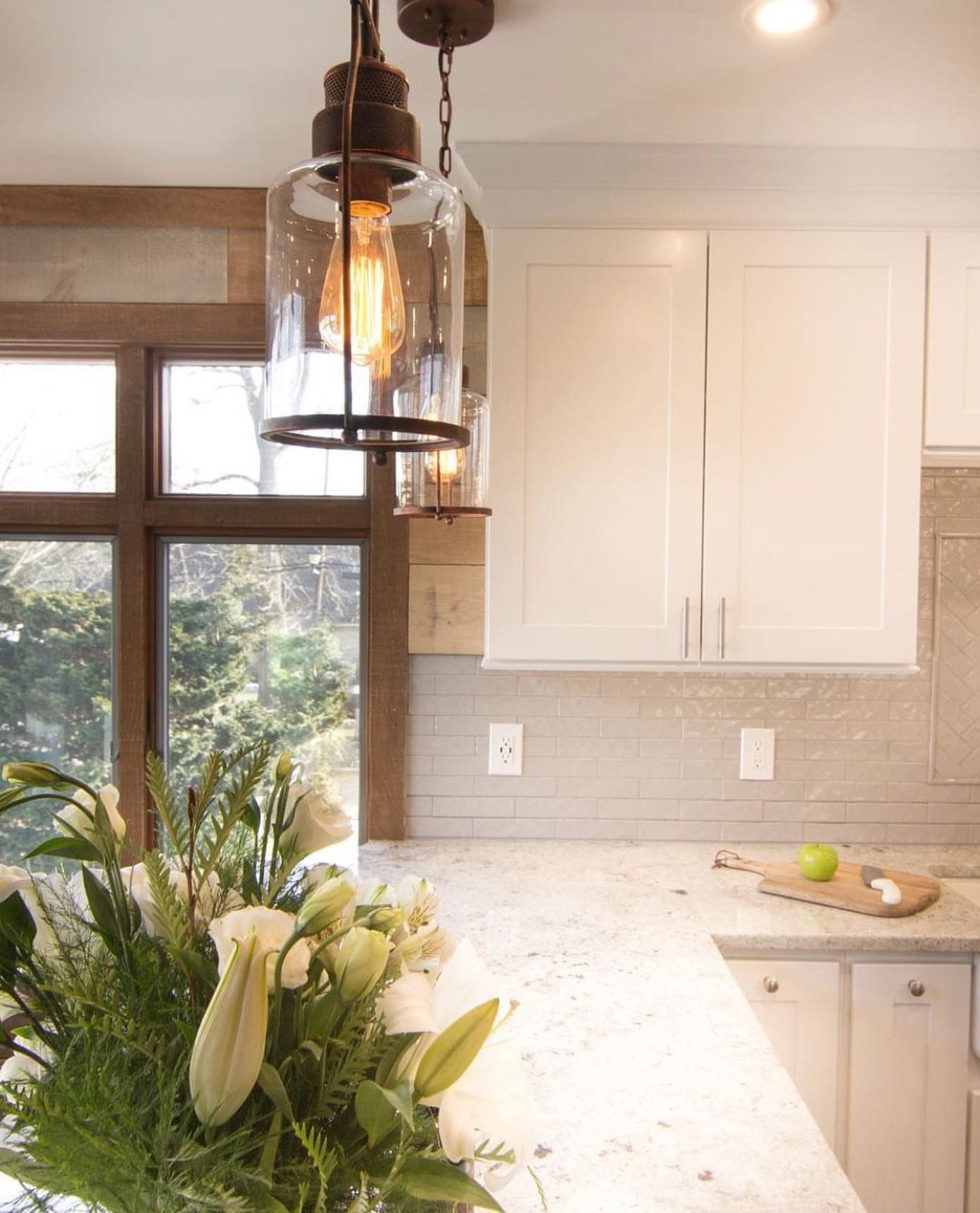 Kitchen with white cabinets, speckled countertops, glass pendant lights, and a window overlooking greenery.