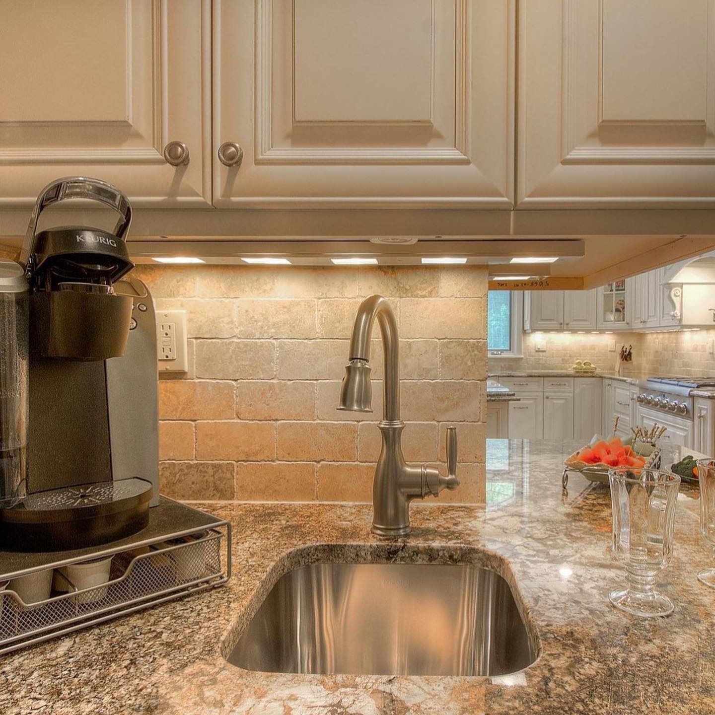 Kitchen sink with a faucet, coffee maker, and cabinets. Countertop, and tiled backsplash.