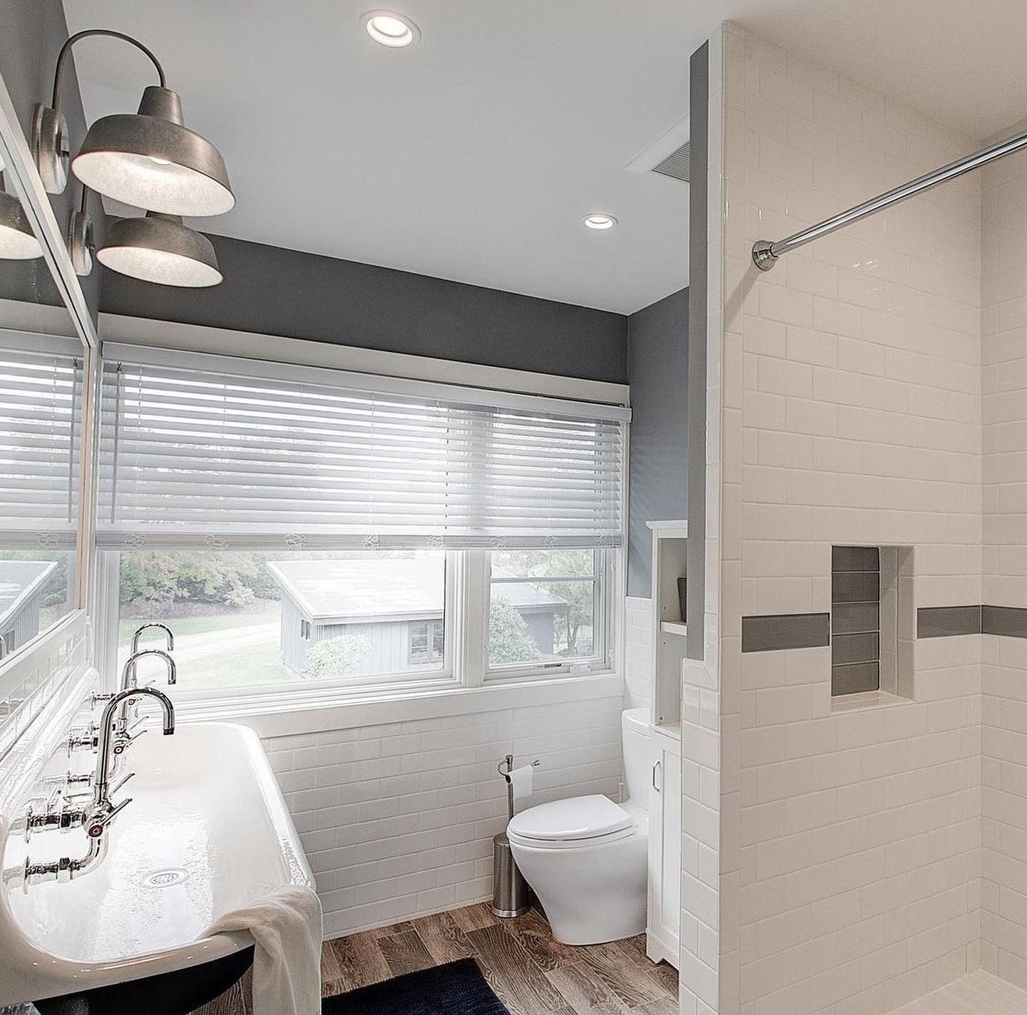 Bathroom with white tile shower, window, and sink with gray accents.