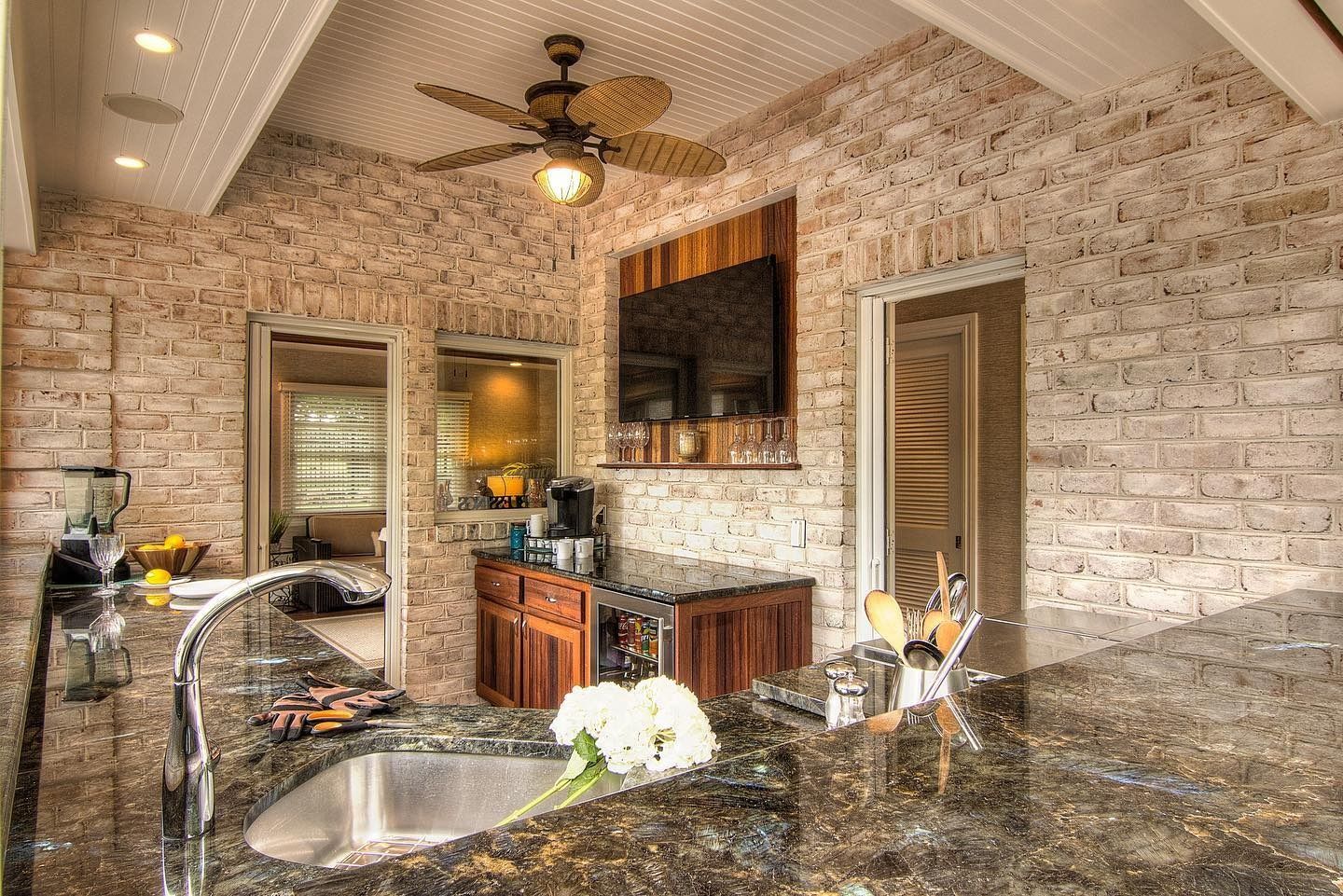 Bar area with brick wall, granite countertop, sink, TV, mirror, and ceiling fan.