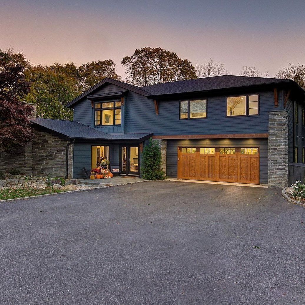 Two-story blue house with wooden garage door, stone accents, and paved driveway, at dusk.
