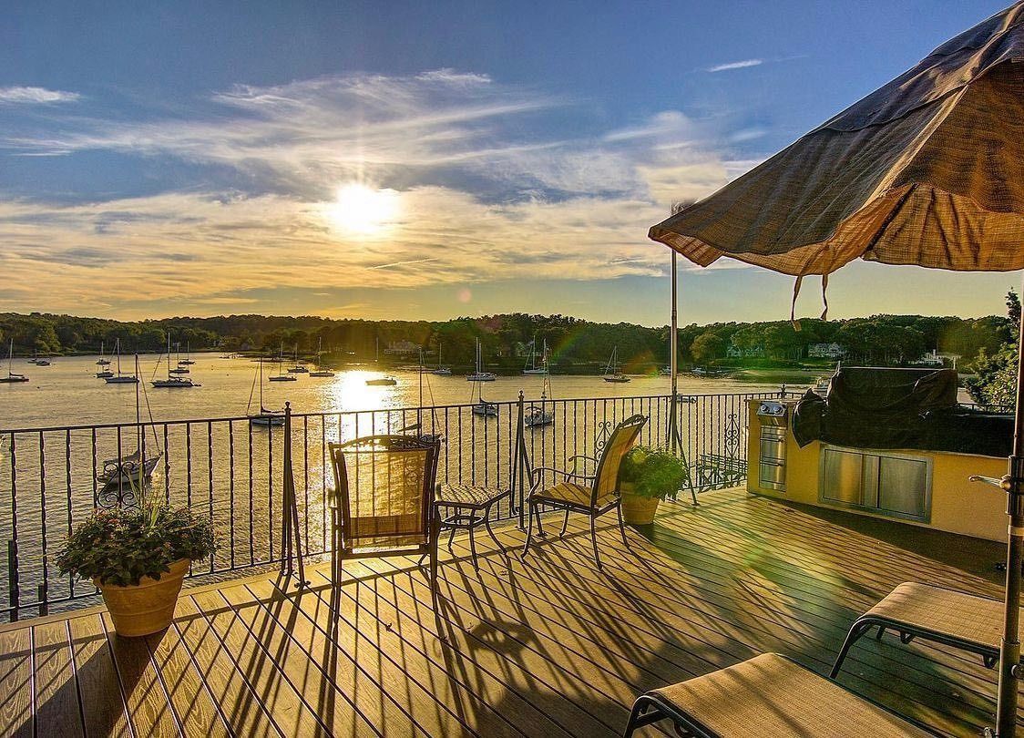 Sunset view from a deck over a harbor with boats; golden light, shadows, and an umbrella.