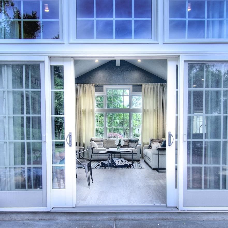 Glass doors open to a living room with white walls, light-colored furniture, and large windows.
